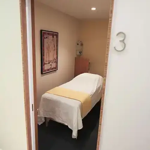 oom with a massage table covered in a white and yellow sheet, a framed picture on the wall, and the door marked with the number '3.'
